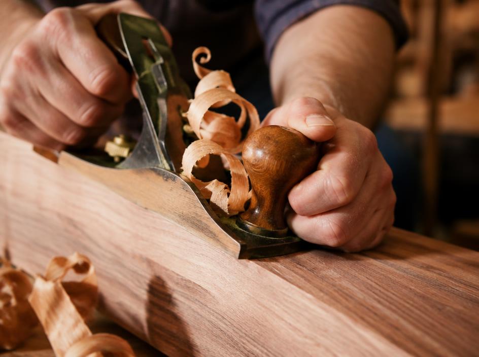 A hand plane gliding over a walnut surface with curling wood shavings